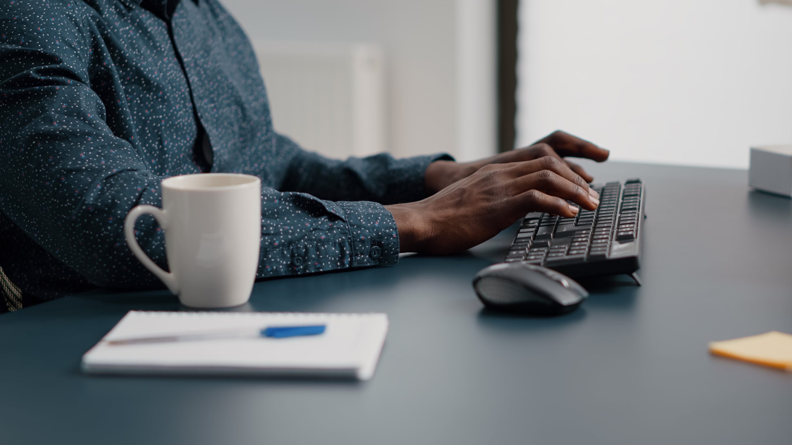 Close up of african american man hands typing on computer keyboard in living room, using internet online web communication from home office. Remote worker working from home